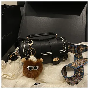 Black cylindrical handbag with gold studs, colorful strap, and plush monster charm in a gift box