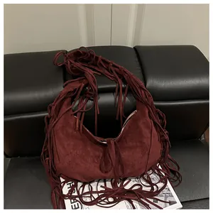 Détail du sac croissant en daim bordeaux avec de longues franges sur un siège