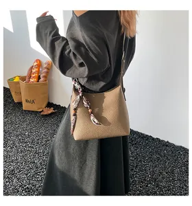 Detail of khaki litchi texture shoulder bag with decorative silk scarf on model
