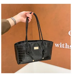 Detail of black crocodile texture handbag with golden metal plate and slim shoulder straps