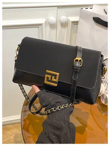 Detail of black leather small square bag featuring a gold geometric metal buckle and chain strap