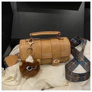 Brown cylinder handbag with gold rivets and colorful patterned wide shoulder strap