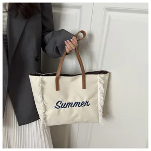 Détail du sac fourre-tout en toile crème avec broderie Summer bleue et glands blancs