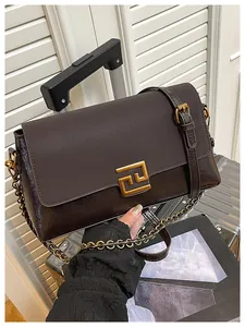 Detail of dark brown leather handbag with gold buckle leaning against a silver suitcase