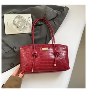 Close-up of luxury burgundy crocodile-embossed tote bag with golden metal hardware detail