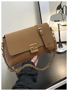 Detailed close-up of brown leather handbag with gold geometric buckle and chain strap