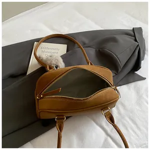 Caramel suede underarm bag with gold hardware and plush ball charm on white sheets