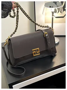 Detail of dark brown leather crossbody bag featuring gold geometric buckle and chain strap