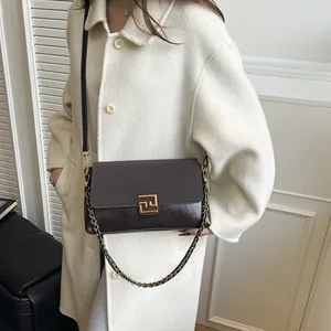 Brown leather crossbody bag with metal buckle and chain strap on stylish beige coat