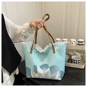 Detalle del bolso tote de lona azul claro con estampado floral y flecos blancos