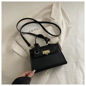 Detail of black lychee grain leather handbag with gold metal clasp on beige suit