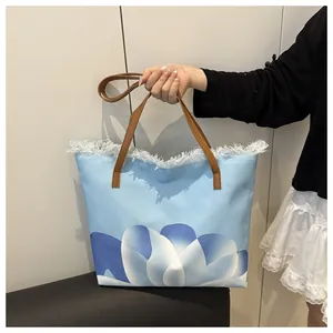 Vista de cerca del bolso de lona con estampado floral azul, bordes deshilachados y asas marrones