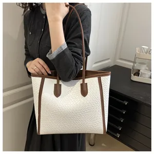 Détail du sac cabas tissé beige avec bordure en cuir marron porté à l'épaule