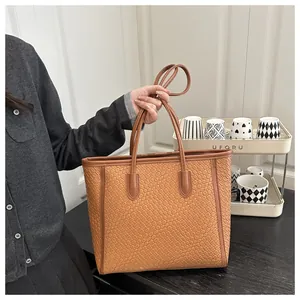 Détail d'un sac cabas marron en cuir PU tressé tenu par un mannequin en intérieur