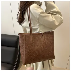 Détail d'un sac cabas tissé marron foncé porté à l'épaule par un mannequin en trench