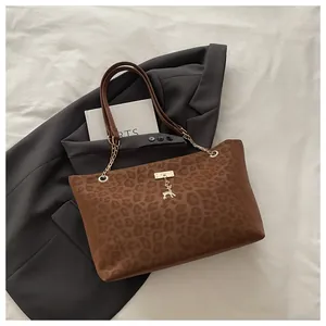 Dettaglio della borsa tote leopardata con ciondolo dorato e tracolla a catena su blazer