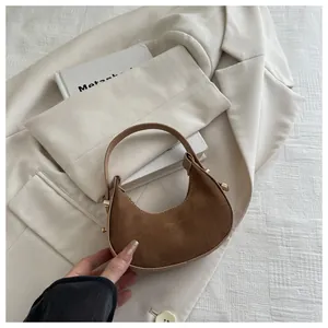 Detail of a brown suede crescent bag with gold hardware on a stylish lifestyle background
