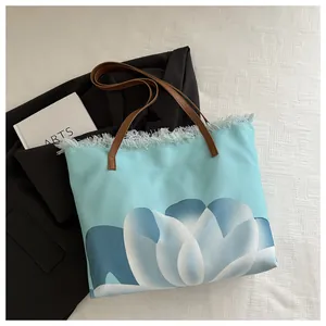 Detalle del bolso tote tie-dye azul con bordes deshilachados y asas de cuero