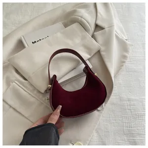 Top-down view of a burgundy suede crescent handbag on a beige suit jacket