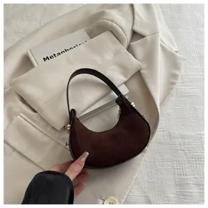 Detail of a dark brown suede crescent bag with leather handle and gold hardware detail