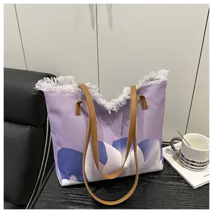 Detalle de bolso tote de lona morada con bordes deshilachados, flores y asas de cuero