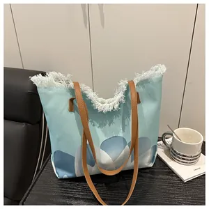 Detalle del bolso tote de lona azul con bordes de flecos blancos y asas de cuero marrón