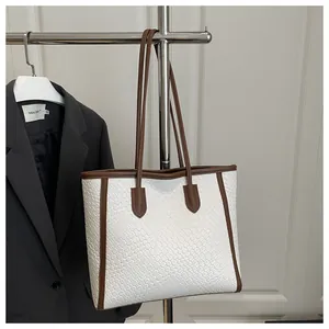 Détail de la texture tressée et des coutures marron sur un grand sac cabas blanc
