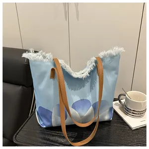 Detalle de bolso tote de lona floral azul con bordes deshilachados y asas de cuero sintético