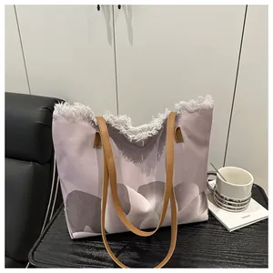 Detalle del bolso tote de lona con estampado degradado lila y borde blanco deshilachado