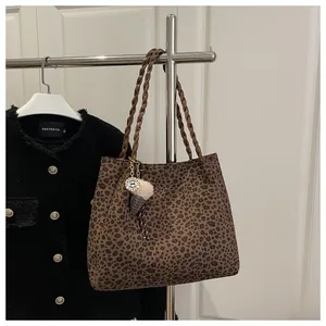 Detailed view of leopard print tote bag with braided handles and a plush charm