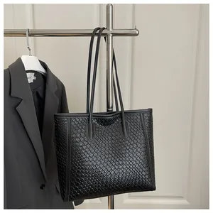 Détail de la texture tressée noire d'un grand sac cabas suspendu à un cintre argenté