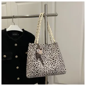 Detail of leopard print tote bag with woven handles and plush charm hanging on a hanger