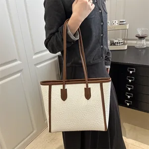 Sac fourre-tout tissé blanc et marron porté à l'épaule par un mannequin en intérieur