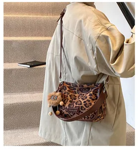 Détail d'un sac bandoulière léopard avec bandoulière en cuir brun et pendentif lion sur mannequin