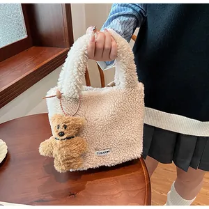 Detail of cream plush faux fur bucket bag featuring a cute brown bear charm on the handle
