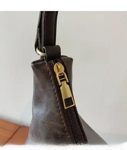 Detail of smooth gold zipper and stitching on dark brown leather shoulder bag