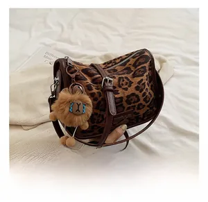 Détail du sac en daim à imprimé léopard avec bordure en cuir marron et breloque lion en peluche