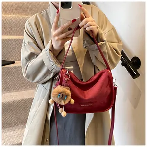 Détail du sac bandoulière bordeaux en daim avec logo argenté et porte-clé lion