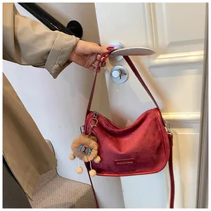Détail du sac à bandoulière en daim bordeaux avec breloque lion et plaque logo en métal