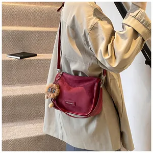 Détail du sac à bandoulière en daim bordeaux avec un joli pendentif lion et logo