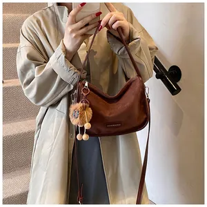 Gros plan d'un sac demi-lune en daim marron avec logo en métal et breloque peluche