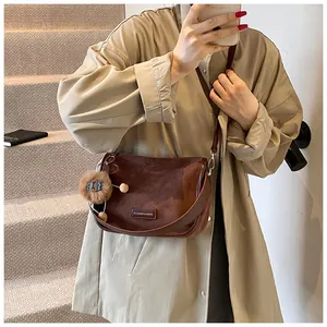 Détail du sac bandoulière en daim marron avec charm lion en peluche et plaque logo