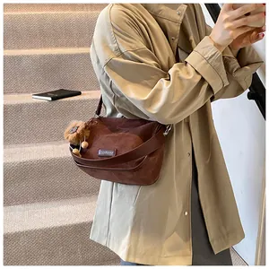 Détail du sac bandoulière en daim marron avec pompon sur un trench-coat beige long