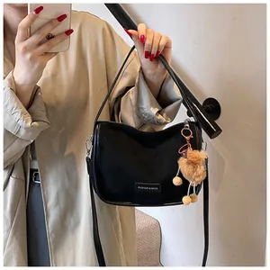 Détail du sac bandoulière noir avec plaque mode et accessoire charm en peluche brune