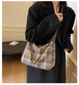 Détail d'un sac seau en laine à carreaux avec chaîne dorée et bandoulière sur modèle