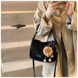 Détail du sac bandoulière en daim noir avec étiquette mode et pompon marron