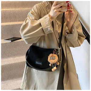 Détail du sac bandoulière noir en toile avec breloque lion sur trench-coat beige