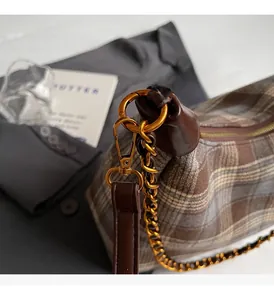 Détail de la chaîne dorée et bordure en cuir sur un sac à bandoulière en laine à carreaux