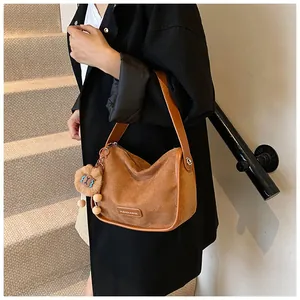 Détail d'un sac bandoulière en daim marron avec pendentif lion sur un manteau noir