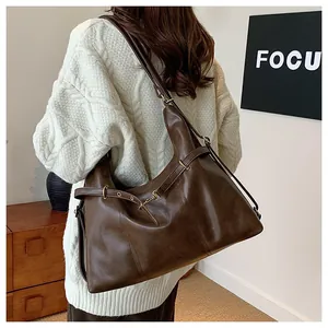 Detail of a large dark brown faux leather tote bag worn with a white knitted sweater